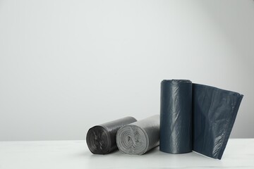 Rolls of different color garbage bags on table against light background. Space for text