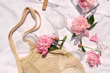 Flat lay composition with beautiful peonies and wineglasses on white fabric