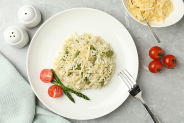 Delicious risotto with asparagus and tomatoes on grey marble table, flat lay