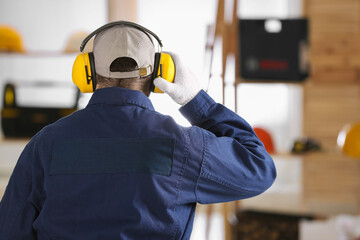 Worker wearing safety headphones indoors, back view. Hearing protection device - obrazy, fototapety, plakaty
