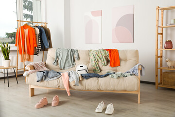 Messy pile of clothes on sofa and shoes in living room