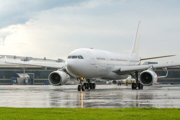 Fototapeta na wymiar An unmarked white passenger jet on an airport apron. White plane in the parking lot at the terminal during the rain. Commercial passenger air transportation