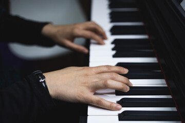 Fototapeta na wymiar Close up of woman's hands playing piano by reading sheet music. Dark mood.