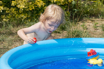 A little boy is playing in the inflatable pool in the summer garden