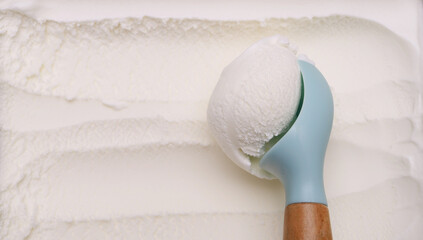 Close-up of coconut milk ice cream scooped out of the container with a blue-handled spoon.