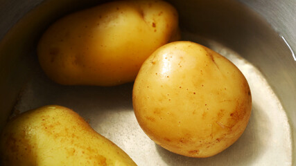 Close-up of golden yellow potatoes soaked in water in a pot.