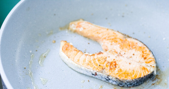 Close-up photo of salmon grilled in pan on blue background.