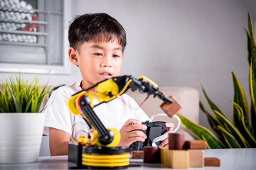 Happy Asian little boy using remote control playing robotic machine arm for pick up wood block, Funny learning successful getting a lesson control robot arm, Technology science education concept