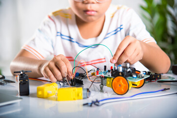 Asian kid boy plugging energy and signal cable to sensor chip with Arduino robot car, Little child...