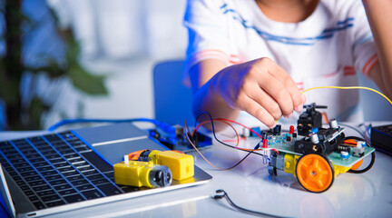 Asian kid boy plugging energy and signal cable to sensor chip with Arduino robot car, Little child...