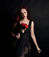 close up portrait of beautiful woman with red hair, wearing black dress with  elegant gestural hand poses on a dark studio background with moody lighting.