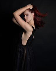 Naklejka premium close up portrait of beautiful woman with red hair, wearing black dress with elegant gestural hand poses on a dark studio background with moody lighting.