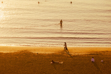 people walking and swimming at the beach during the sunset