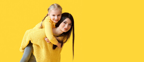 Happy mother and her little daughter in warm sweaters on yellow background with space for text