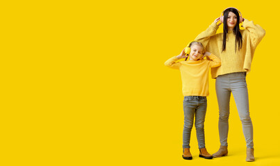 Happy mother and her little daughter in warm sweaters listening to music on yellow background with...