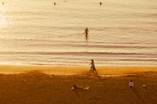 people walking and swimming at the beach during the sunset