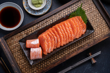 Sliced ​​Fresh Salmon black plate on wooden background, Salmon sashimi salmon sashimi with sauce and wasabi on black background. - obrazy, fototapety, plakaty