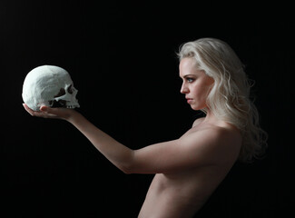 close up portrait of beautiful blond woman holding a human skull, isolated on dark studio...
