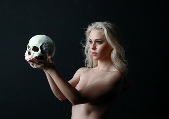 close up portrait of beautiful blond woman holding a human skull, isolated on dark studio...