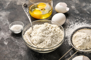 Fototapeta na wymiar Bowl with flour and eggs on dark table, closeup