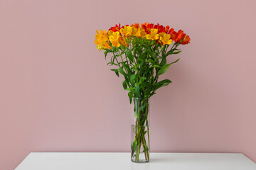 Vase with bunch of alstroemeria flowers on table near color wall