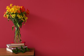 Stack of books and vase with alstroemeria flowers on table near color wall
