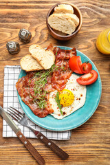 Plate with tasty fried egg, bacon and bread on wooden background
