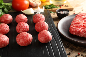 Cutting board with raw meat balls, plate of mince and vegetables on wooden background