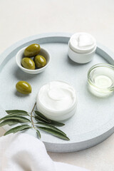 Tray with jars of cream, green olives, oil and plant branch on white background