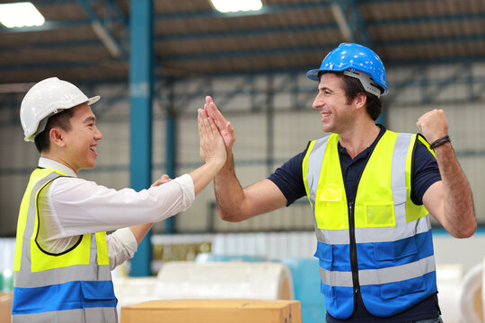 Two technician engineer man in protective uniform with hardhat standing and give high five celebrate successful together or completed deal commitment at industry warehouse manufacturing factory