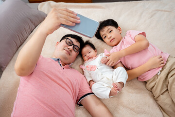 Handsome Asian dad, picks up his phone to take a selfie with his daughter, and son, cutely and warmly, All three wear the same color as a family, The older brother took the sister's hand to play.