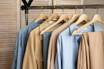 Trendy capsule wardrobe in beige and light blue on a rail rack against the backdrop of a screen.