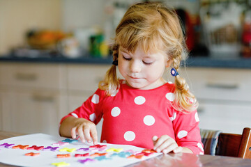 Little toddler girl playing with different colorful stickers and painting flowers. Concept of activity of children during pandemic corona virus quarantine. Child learning colors with parents at home