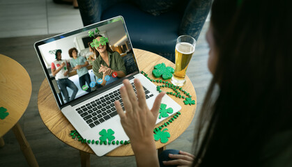 Caucasian woman with beer making st patrick's day video call waving to friends on laptop at bar