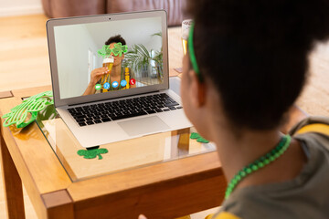Mixed race woman making st patrick's day video call to friend in costume on laptop at home