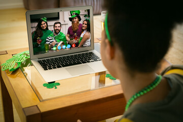 Mixed race woman making st patrick's day video call to friends in costume on laptop at home