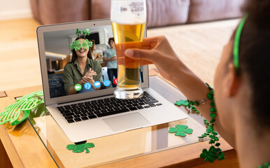 Naklejka na ściany i meble Mixed race woman with beer having st patrick's day video call with female friend on laptop at home