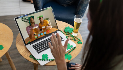 Fototapeta na wymiar Caucasian woman at bar making st patrick's day video call waving to friends in costumes on laptop