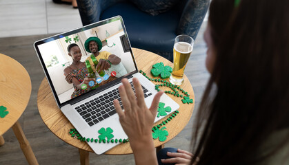Fototapeta na wymiar Caucasian woman at bar making st patrick's day video call waving to friends in costumes on laptop
