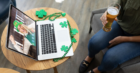 Mixed race woman holding beer at bar making st patrick's day video call with friend on laptop - Powered by Adobe