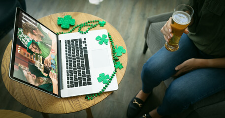 Mixed race woman holding beer at bar making st patrick's day video call with friends on laptop - Powered by Adobe
