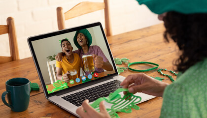Mixed race woman making st patrick's day video call to male friends drinking beer on laptop at home