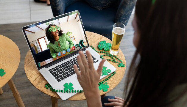 Caucasian woman at bar making st patrick's day video call waving to friend in costume on laptop