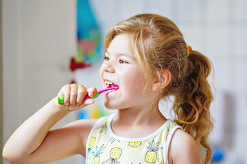 Cute little girl with a toothbrush and toothpaste in her hands cleans her teeth and smiles. Happy preschool child brushing first teeth.