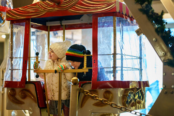 Little preschool girl riding on ferris wheel carousel horse at Christmas funfair or market, outdoors. Happy toddler child having fun on traditional family xmas market in Germany