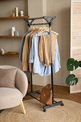 Trendy capsule wardrobe in beige and light blue on a rail rack against the backdrop of a screen in a modern living room.