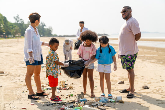 Group Of Diversity Family On Summer Holiday Vacation. Parents Teaching Children Kid Picking Up Plastic Bottle And Garbage On The Beach. Environment Protection Volunteer And Waste Pollution Concept