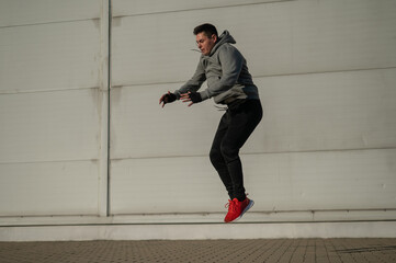 Caucasian man in hoodie jumping high with hands on knees outdoors. 