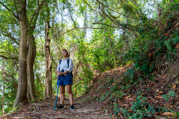 Naklejka na ściany i meble Happy Asian woman traveler on summer holiday travel vacation. Mature adult woman hiking in rain forest. Attractive female enjoy outdoor lifestyle trekking and looking to green trees on the mountain