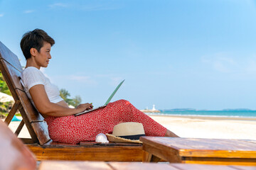 Modern Asian businesswoman working on laptop computer with internet at tropical beach in summer...